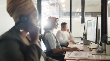 Drei Personen sitzen im Kundenservice an Laptops und Telefonen