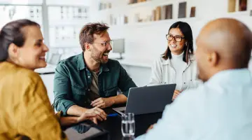 Vier Geschäftsleute sitzen an einem Tisch um einen Laptop herum